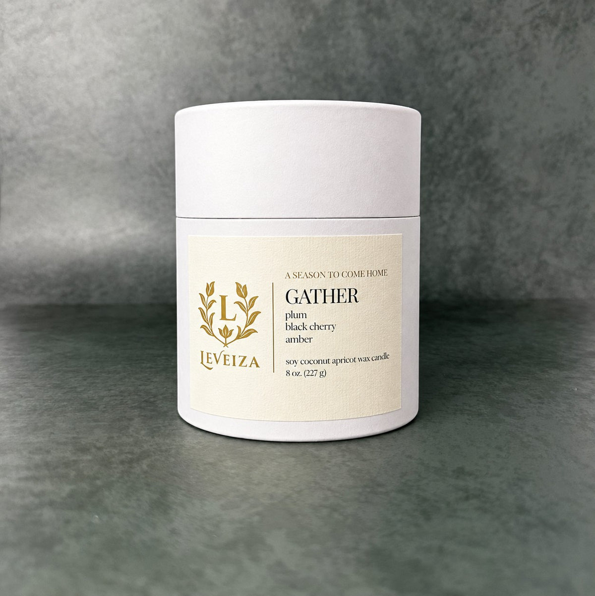 White Leveiza Gather candle tube with a label listing plum, black cherry, and amber scent notes