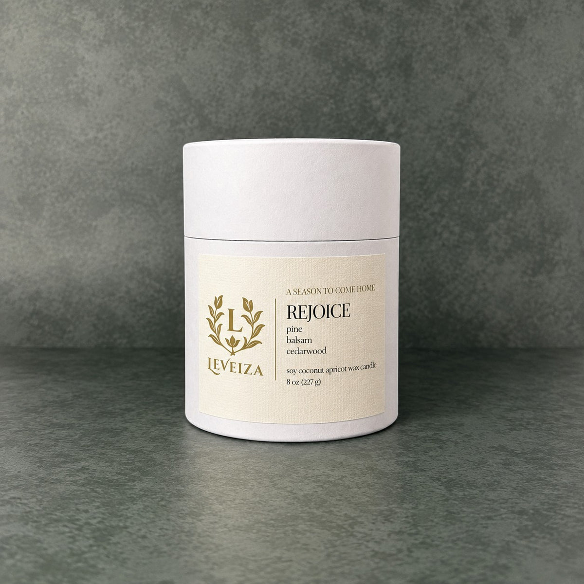 White Leveiza Rejoice candle tube with a label listing pine, balsam, and cedarwood scent notes