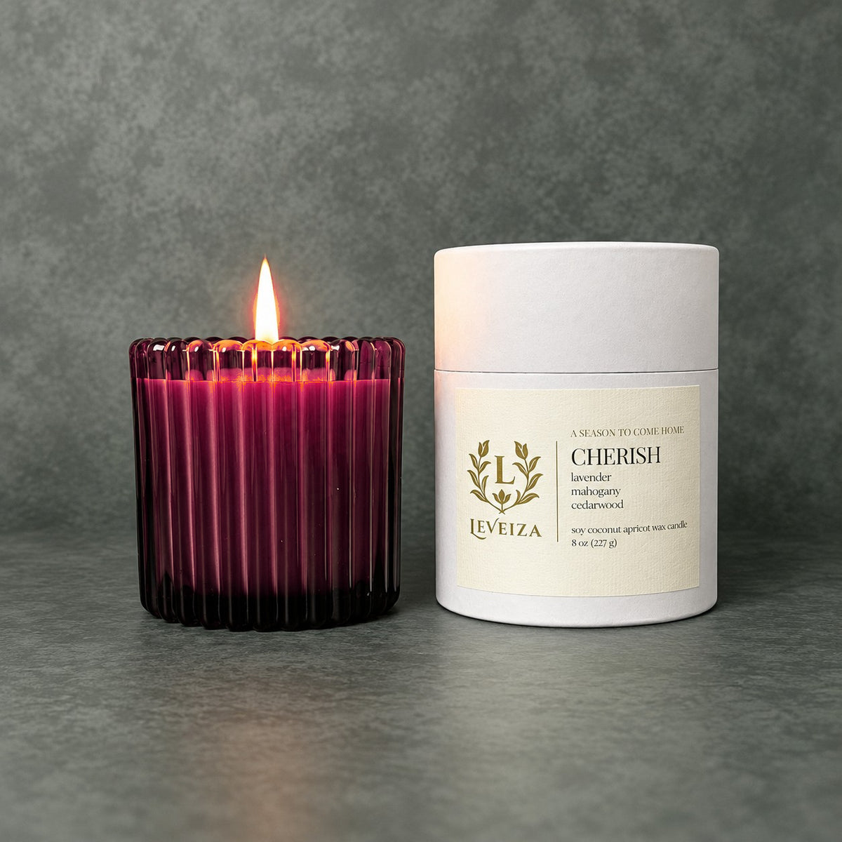 Lit Cherish scented candle by Leveiza in deep plum ribbed glass beside its white labeled tube packaging
