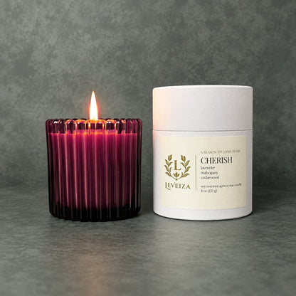 Lit Cherish scented candle by Leveiza in deep plum ribbed glass beside its white labeled tube packaging
