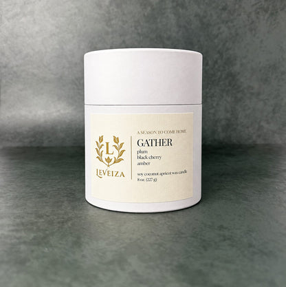 White Leveiza Gather candle tube with a label listing plum, black cherry, and amber scent notes
