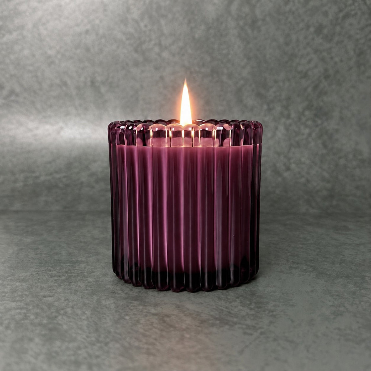 Lit candle in a deep plum ribbed glass vessel against a textured gray background.
