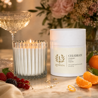 Lit Celebrate candle and tube surrounded by champagne, berries and tangerine in an elegant celebration setting.
