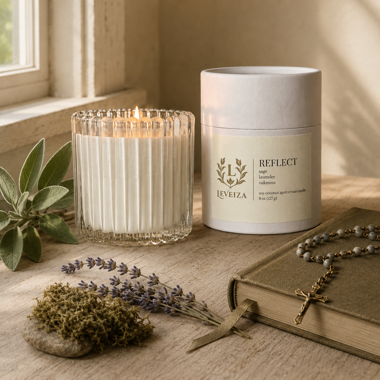 Lit Reflect candle and tube beside a Bible, rosary, sage, lavender and oakmoss in a peaceful prayer setting.
