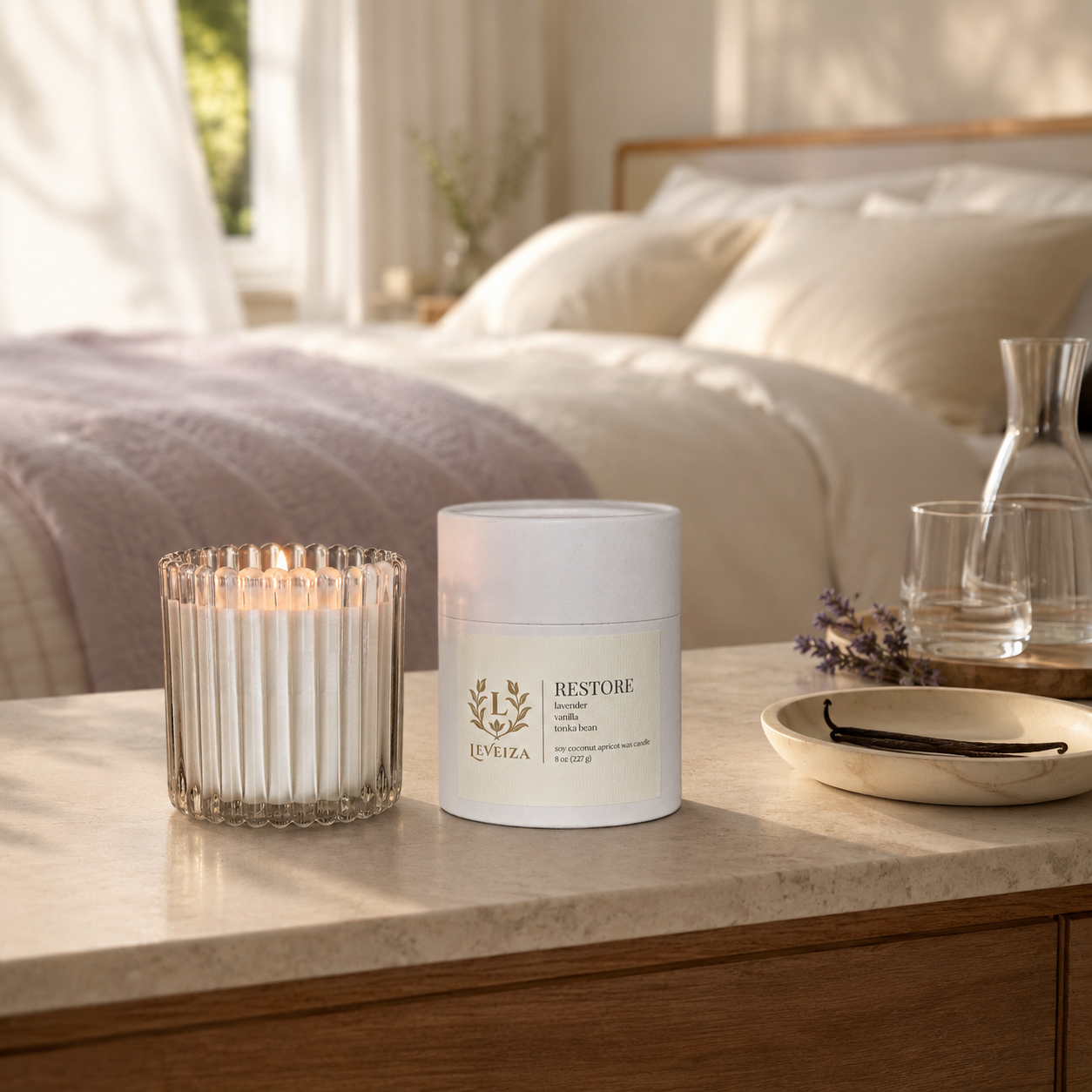 Lit Restore candle and tube with lavender and vanilla on a dresser in a softly lit, restful bedroom.
